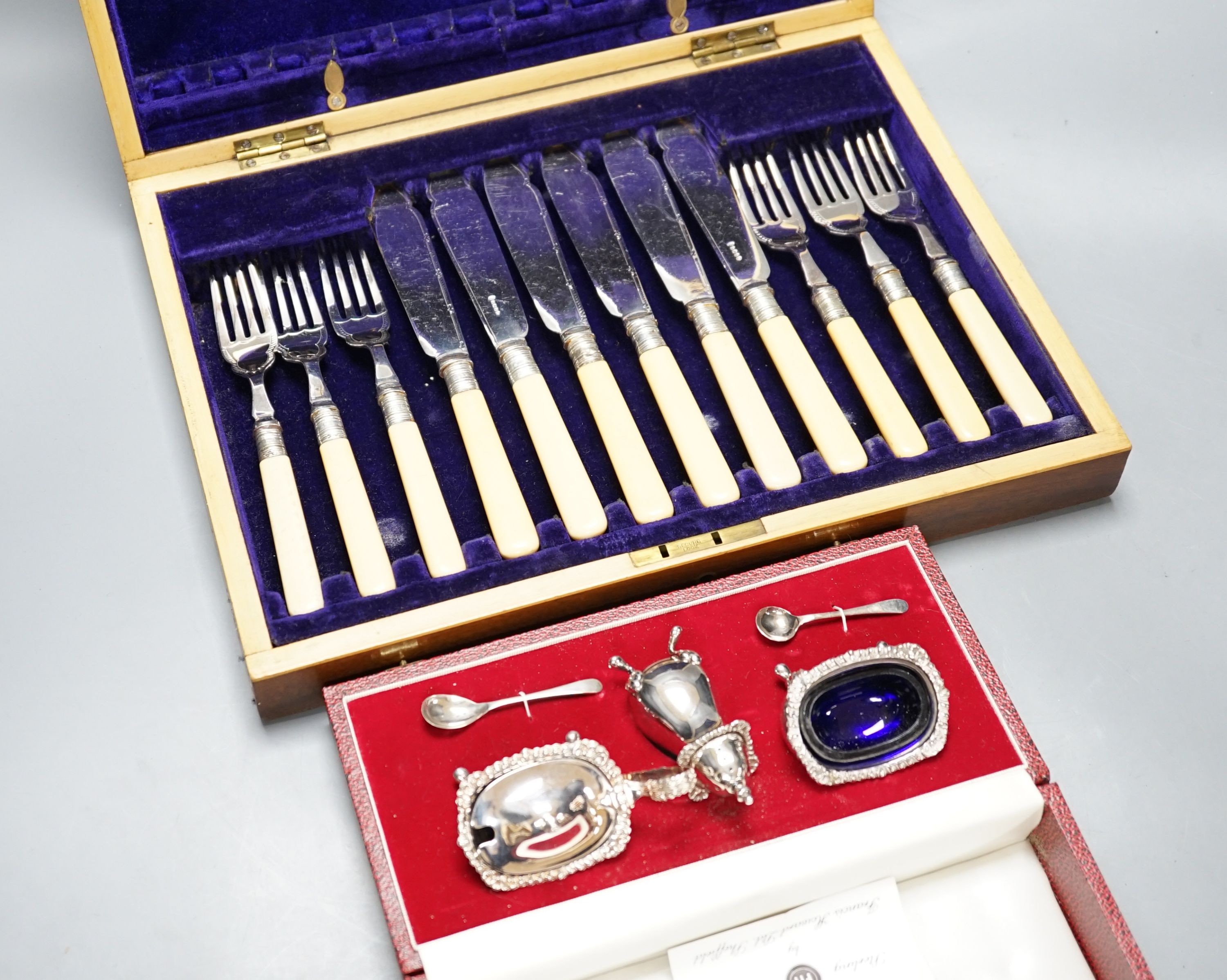 A cased modern silver three piece condiment set, a cased set of twelve Edwardian silver teaspoons, London, 1903 (lacking tongs) and two plated fish services.